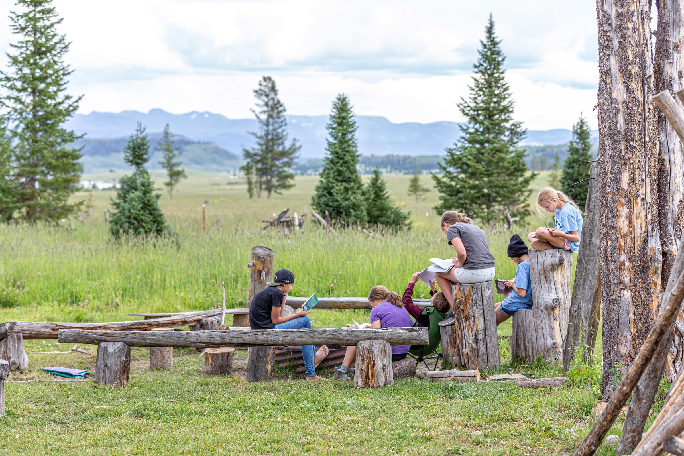 Camp kids reading outdoors in a mountain meadow
