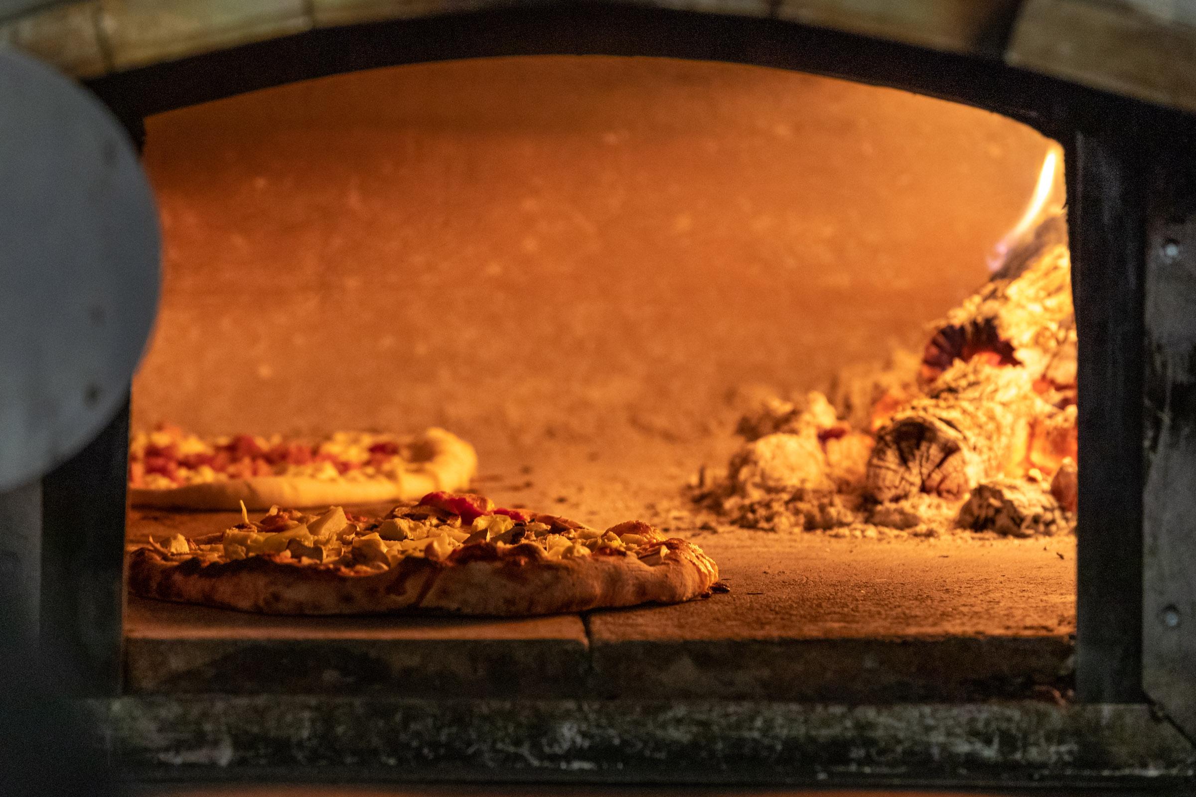 Wood-fired oven with pizzas cooking over open flame